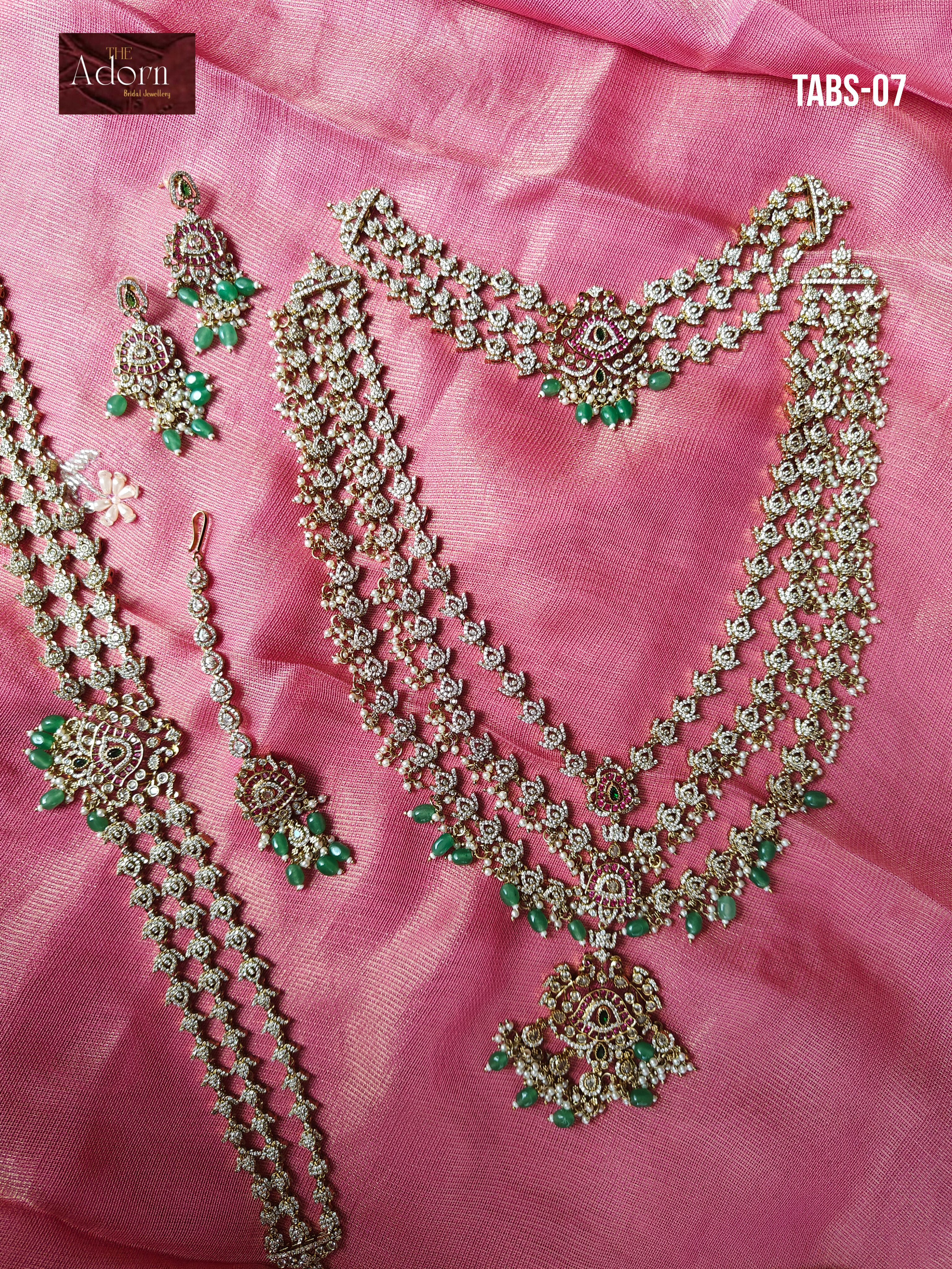 Archive Seven, A layered gold-tone bridal set photographed against rose silk, with cascading stone-set strands, emerald drops and matching earrings, maang tikka and vanki.