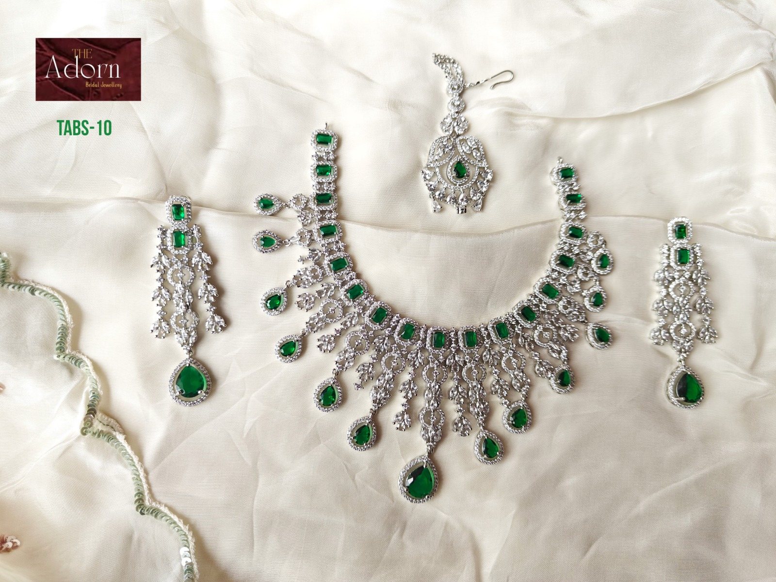 Emerald Cascade, A bright, open silver-tone necklace arranged around rectangular and teardrop emerald-colour stones.
