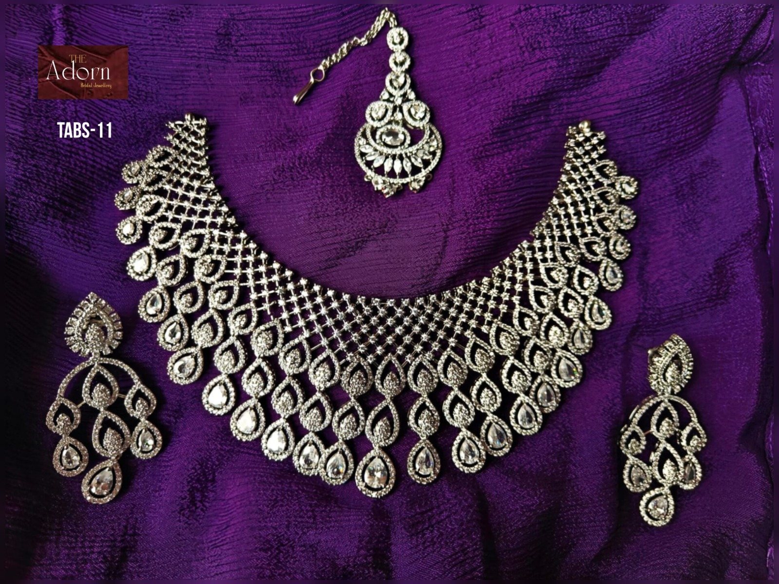 The Crystal Veil, A broad silver-tone collar composed from repeated teardrop forms, accompanied by long statement earrings and a forehead ornament.
